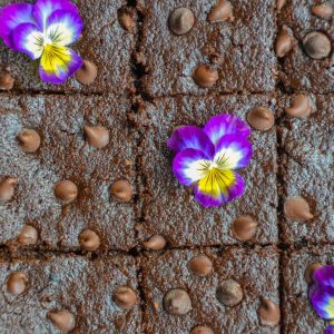 A tray of sliced Fudgy Gluten-Free Brownies topped with chocolate chips and decorated with purple and yellow edible flowers.