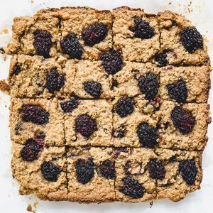 A large tray of baked Blackberry Banana Bread Bars topped with blackberries. The squares are slightly browned, crumbly, and arranged neatly in a grid. The juicy berries are scattered across the surface, adding a burst of dark color.