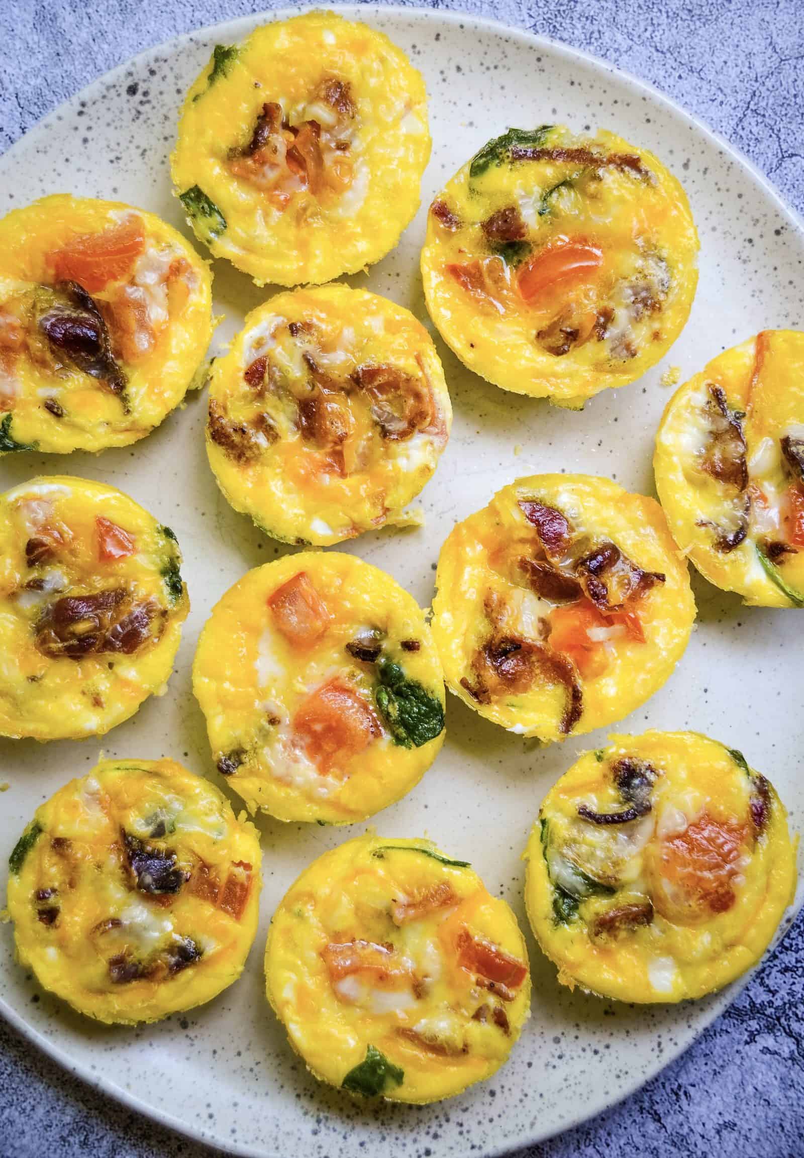 Baked breakfast egg muffins with vegetables and cheese on white plate.