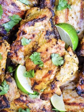 Grilled Tequila Lime Chicken garnished with cilantro and accompanied by lime wedges. The chicken has a golden-brown, charred appearance, highlighting the seasoning and herbs used in its preparation.