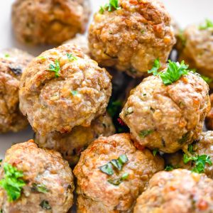 A white plate filled with browned turkey meatballs, garnished with chopped parsley. The meatballs are arranged neatly, showcasing their round shape and slightly crispy exterior.