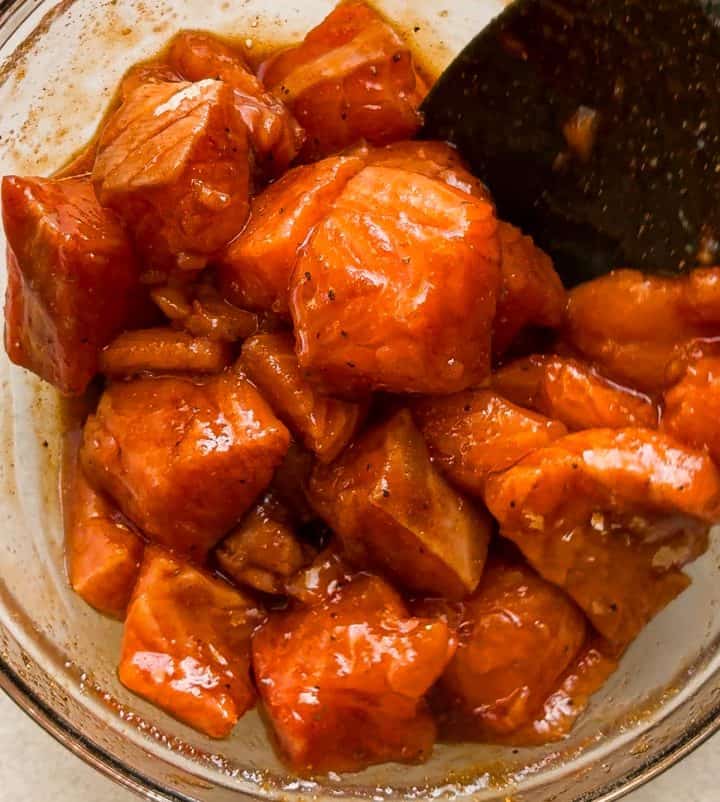 Raw salmon cubes tossed in the honey, soy sauce, sesame, and ginger marinade in a glass bowl before air frying.