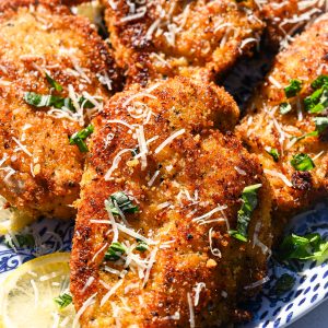 Crispy lemon garlic chicken cutlets topped with parmesan and BASIL on a blue and white plate.