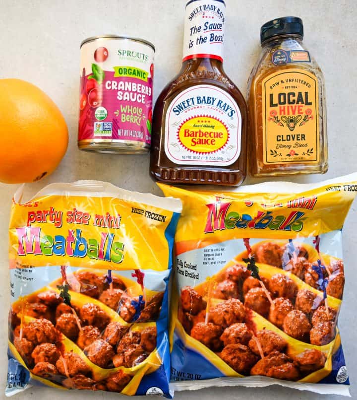 Overhead view of ingredients for holiday meatballs, including frozen meatballs, barbecue sauce, hot honey, orange juice, and seasonings.