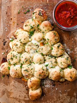 Christmas tree pull-apart garlic bread with melted cheese and marinara dipping sauce on a wooden board.