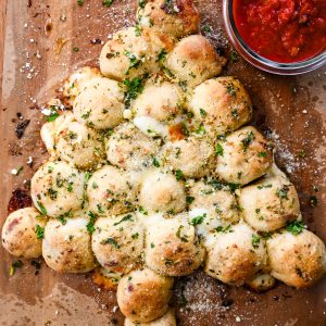 Christmas tree pull-apart garlic bread with melted cheese and marinara dipping sauce on a wooden board.