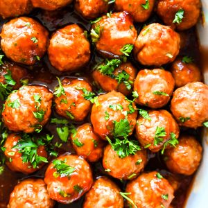 Overhead shot of glazed holiday meatballs topped with fresh parsley, arranged tightly on a baking sheet.