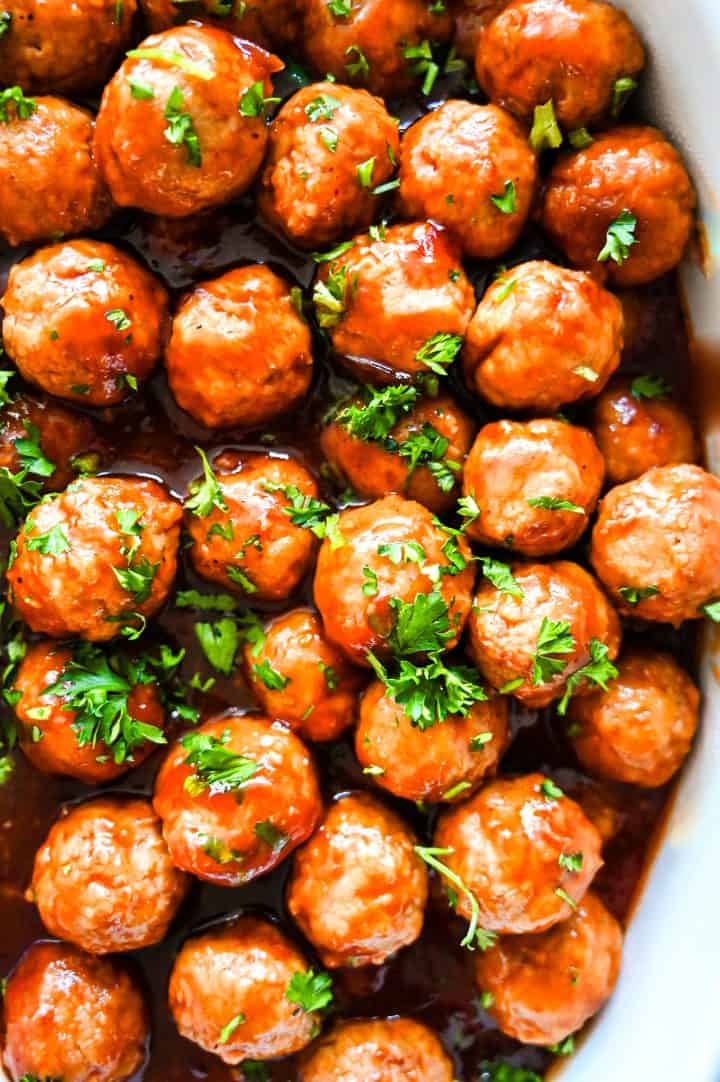 Overhead shot of glazed holiday meatballs topped with fresh parsley, arranged tightly on a baking sheet.