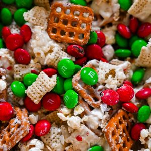 Close-up of Reindeer Crunch Snack Mix with Chex cereal, pretzels, popcorn, white chocolate, crushed peppermint, and red and green Christmas M&M’s.